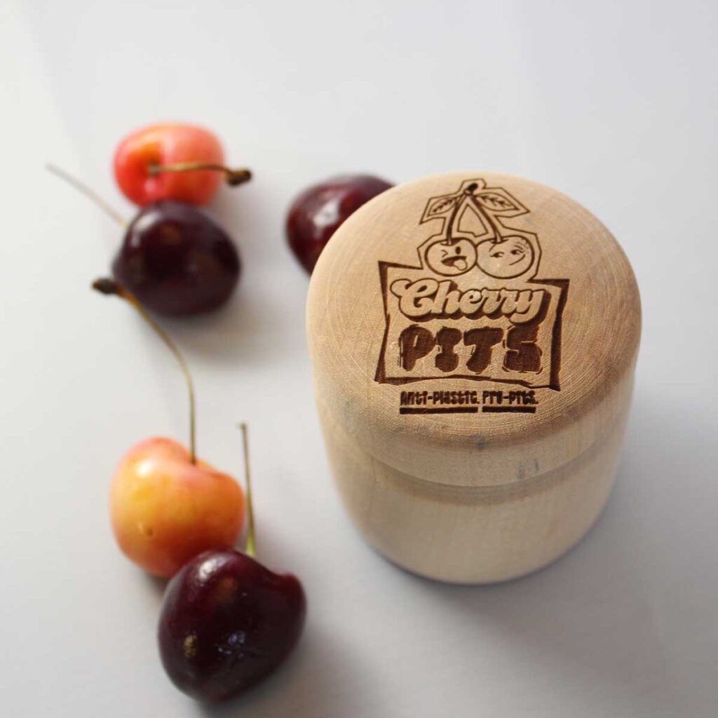 Cherry Pits The Pit Stop, wooden container for deodorant surrounded by cherries with the Cherry Pits logo laser engraved on the lid of the container