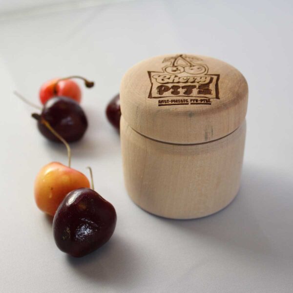 Cherry Pits The Pit Stop, wooden container for deodorant surrounded by cherries with the Cherry Pits logo laser engraved on the lid of the container