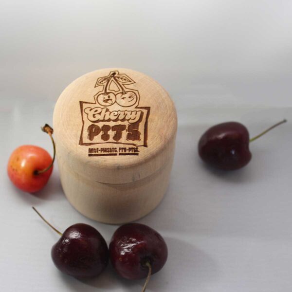 Cherry Pits The Pit Stop, wooden container for deodorant surrounded by cherries with the Cherry Pits logo laser engraved on the lid of the container